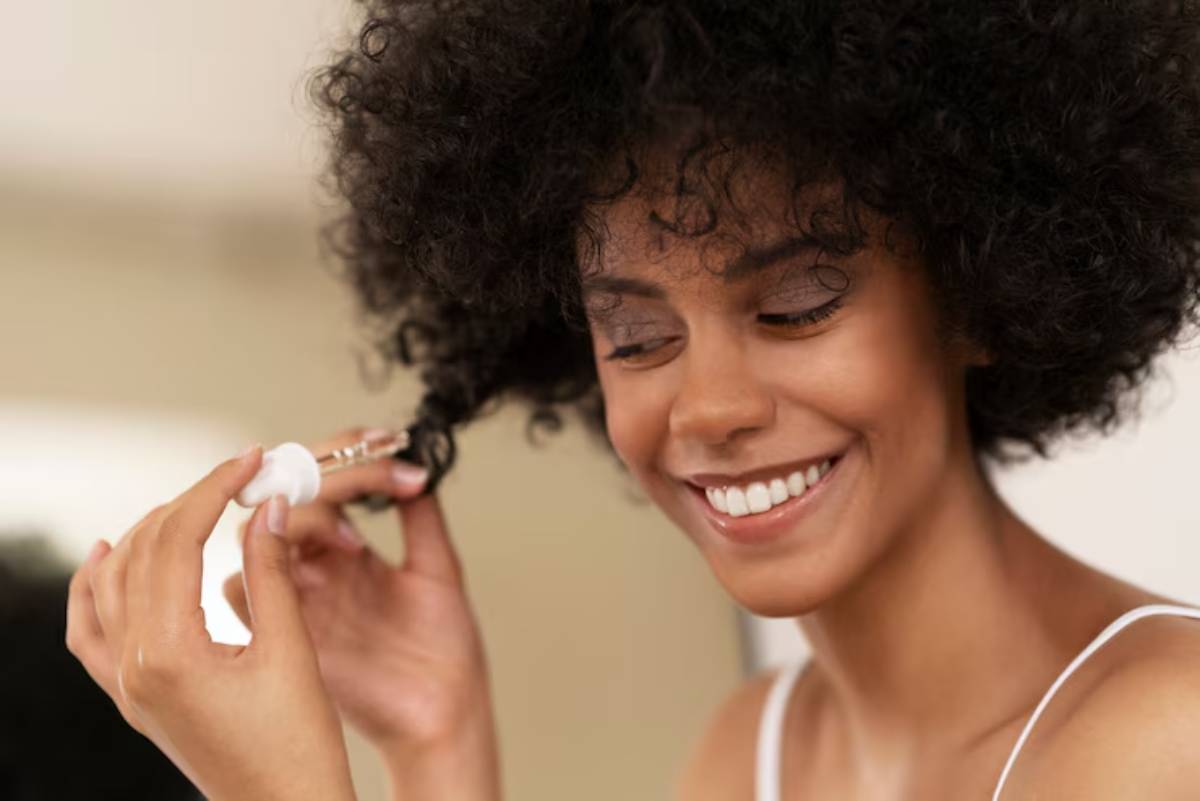 A person with curly hair holds a dropper, applying a hair product. Soft lighting accentuates the textured hairstyle.