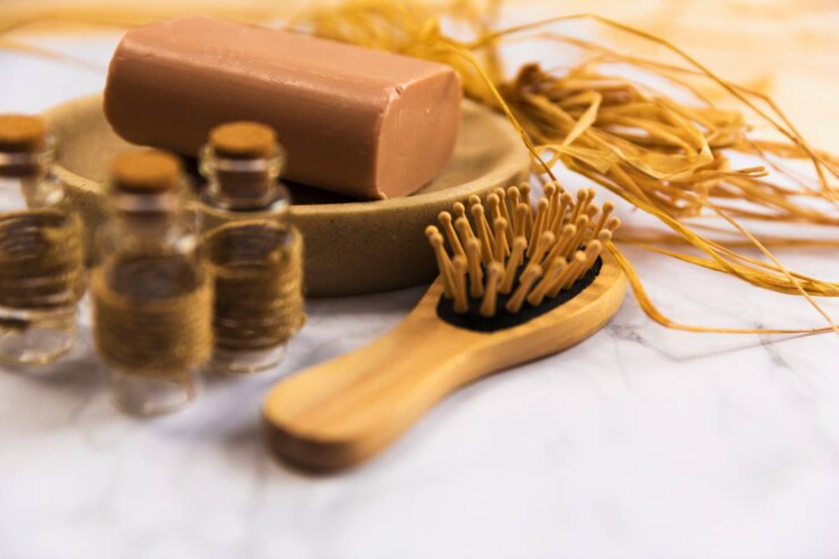 A natural skincare setup featuring a brown soap bar, small glass bottles, a wooden hairbrush, and decorative straw.