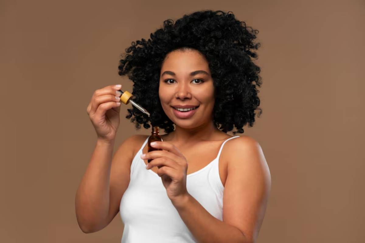 A person holds a dropper bottle with an amber glass container, poised to dispense liquid, set against a warm brown background.