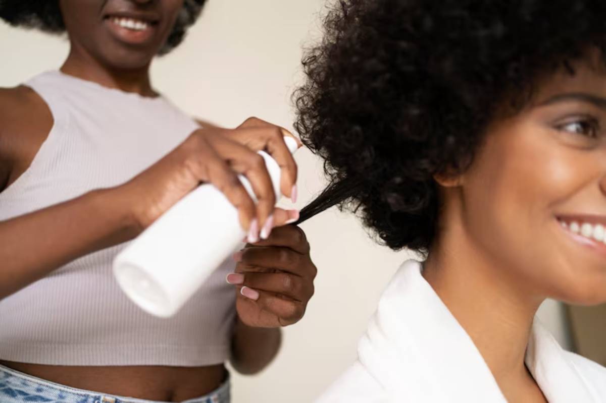 A person applies hair product from a spray bottle to a curly hairstyle, showcasing a focus on hair care.