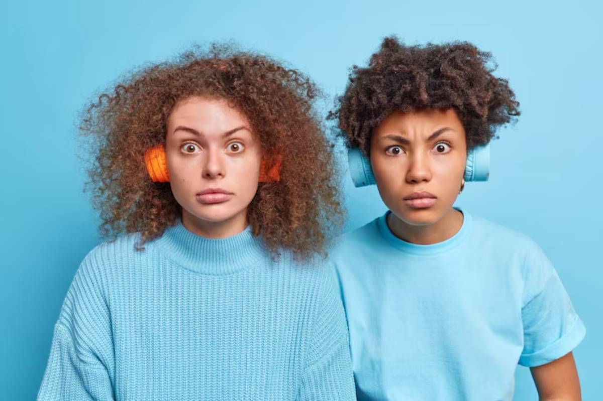 Two children with curly hair wearing colorful headphones, against a bright blue background, both dressed in relaxed pastel outfits.