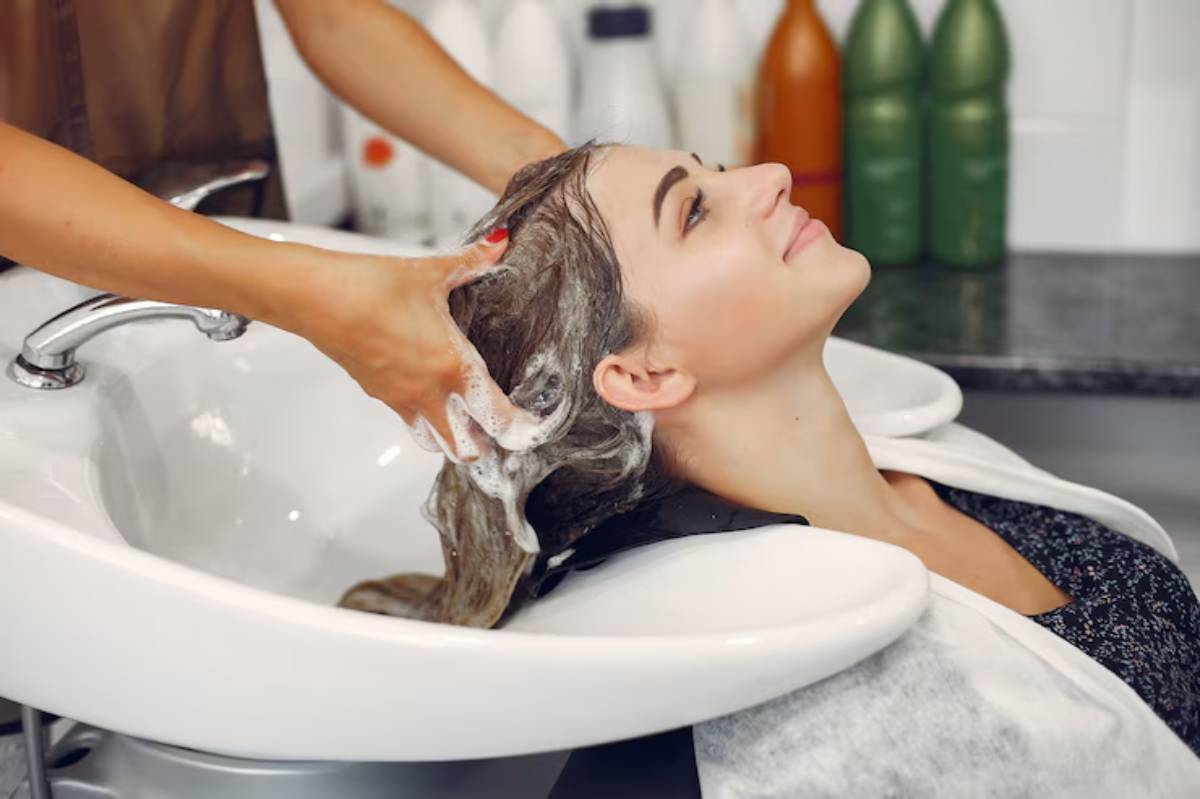 A person receives a shampoo treatment at a salon, with a stylist's hands massaging the scalp near a wash basin.