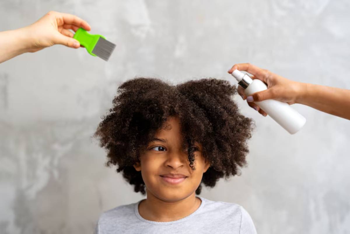 A child with curly hair sits while someone sprays hair product and another holds a green brush for styling.
