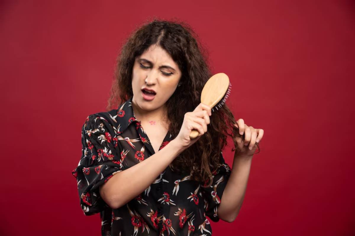 A person with curly hair brushes their hair while wearing a floral-patterned shirt against a vibrant red background.