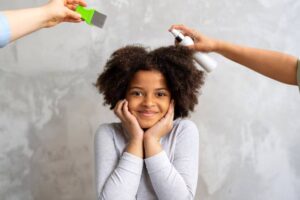 A person with textured hair is having their hair styled, while two hands apply spray and use a green comb.