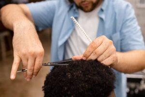 A barber carefully cuts textured hair while holding a comb, focusing intently on the client's style in a well-lit salon.